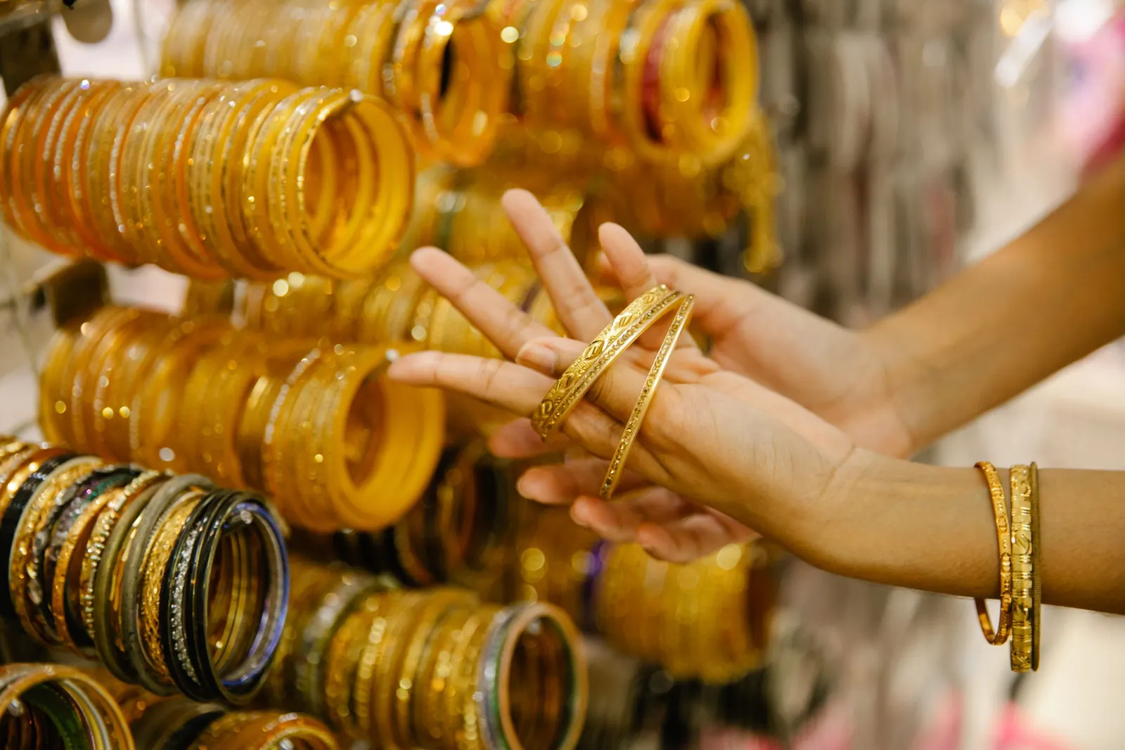 A customer trying on gold bangles at a jewellery counter, with rows of bangles behind