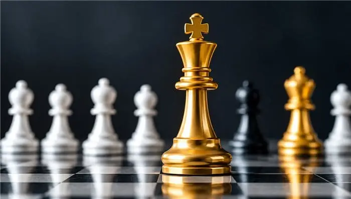 Gold king chess piece standing ahead of silver and black pieces on a chessboard