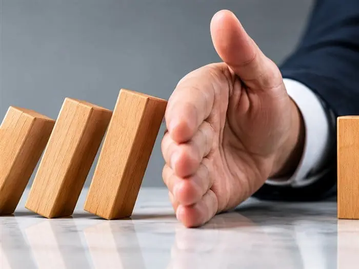 A hand stopping a row of falling dominoes, symbolising risk prevention through strong systems